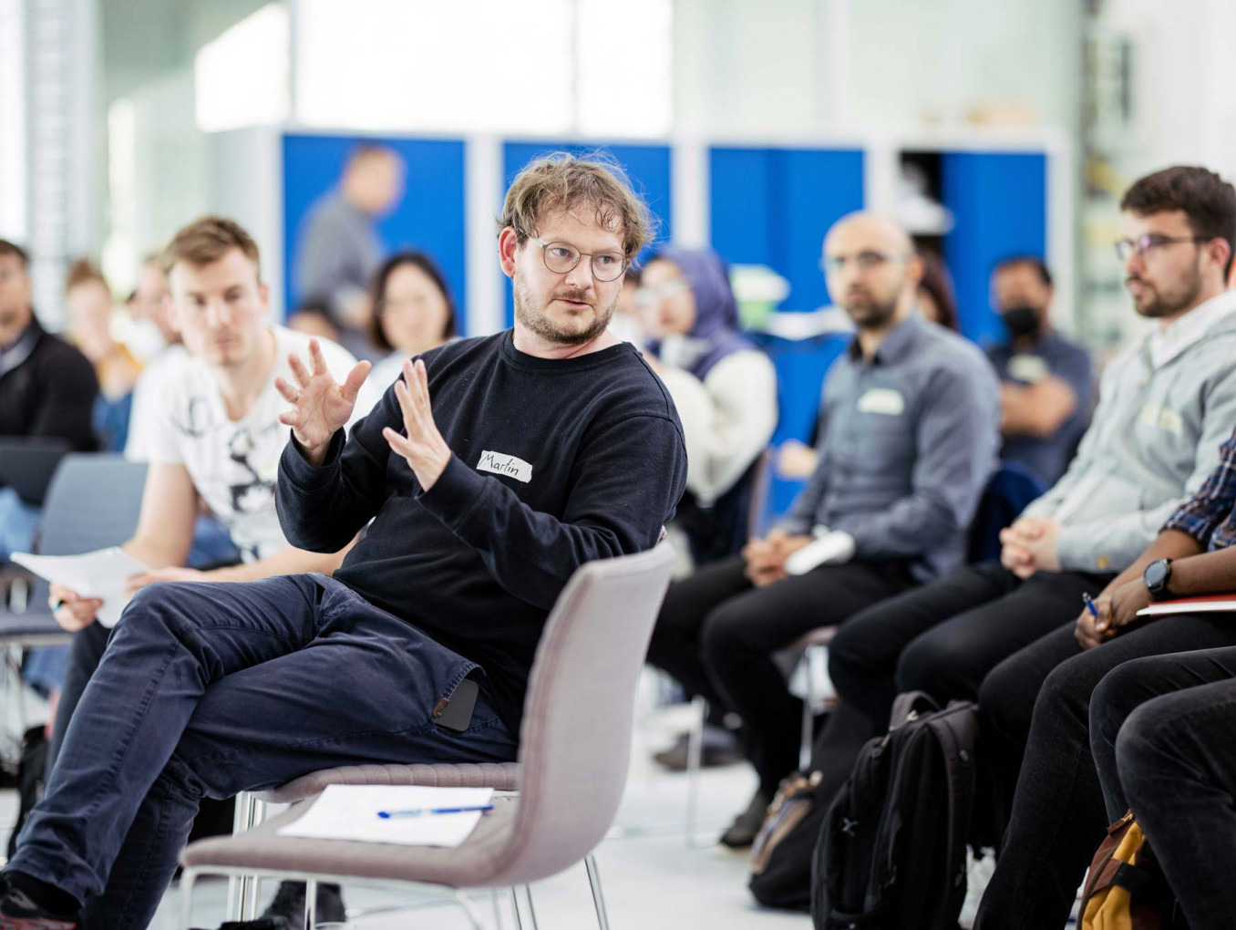 A person speaks while gesturing with hands during a group discussion in a workshop setting.
