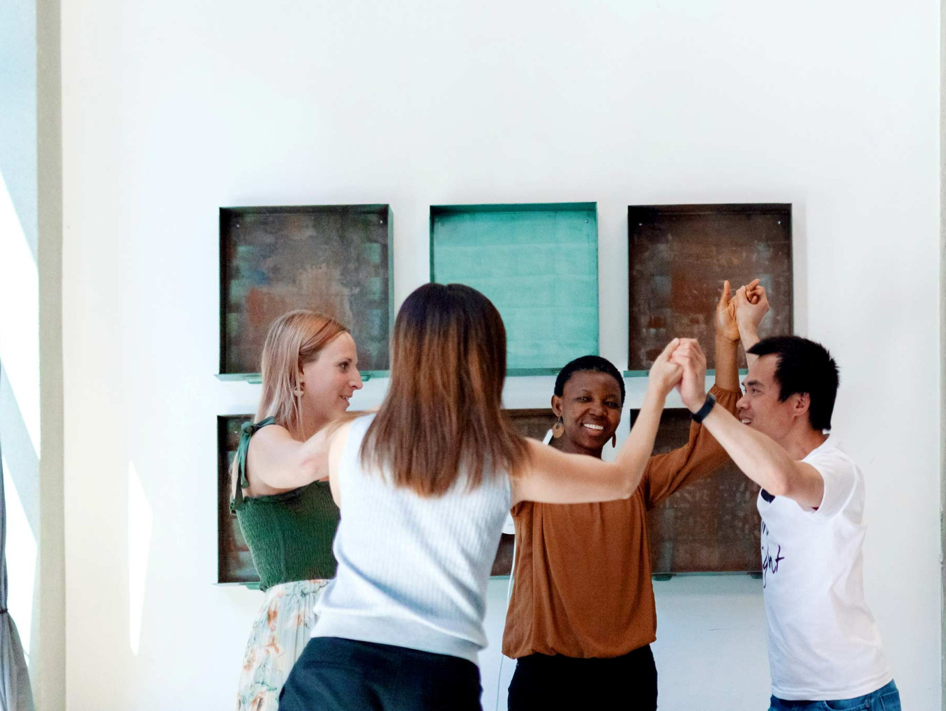 Four people stand in a circle, smiling and raising their hands together in a team activity during a workshop.