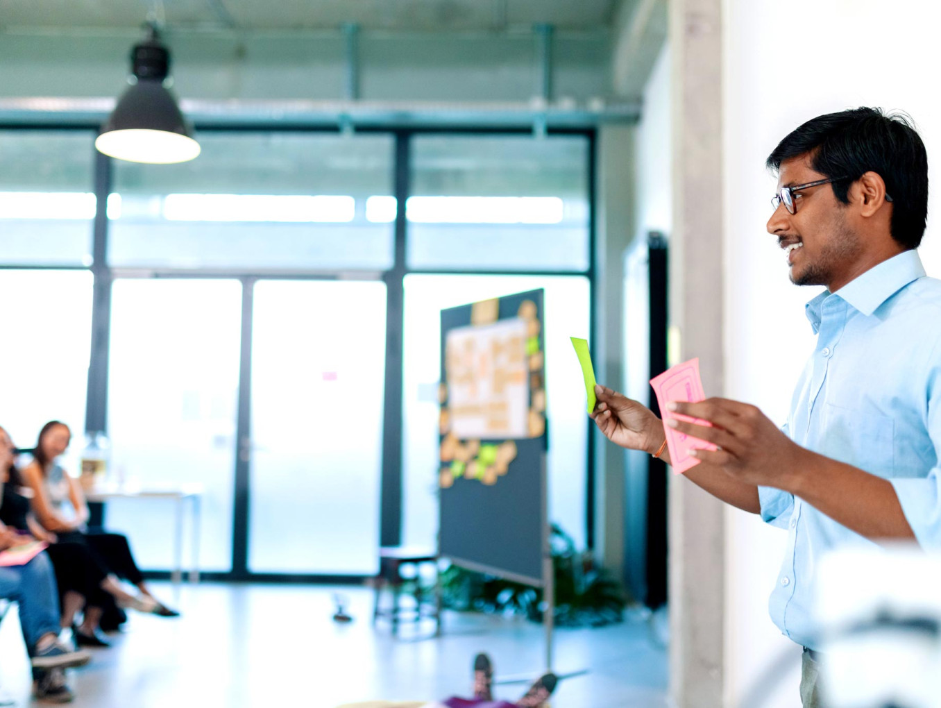A person is presenting with colorful cards in hand, while a small group listens in a workshop setting.
