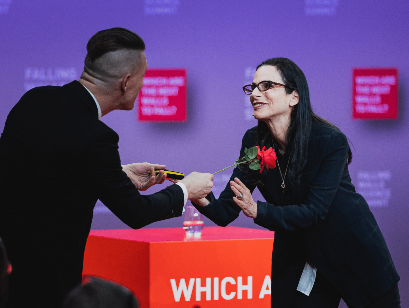 A man gives a single flower to a speaker at the Science Summit stage.