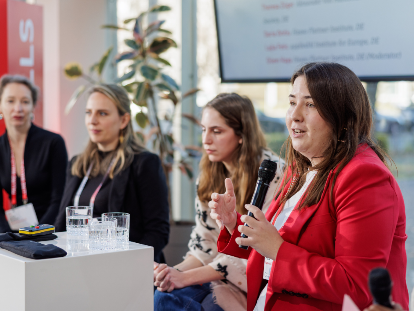 A group of five women scientists are sitting in a row. The second woman from the right is speaking. Everyone is listening to her.