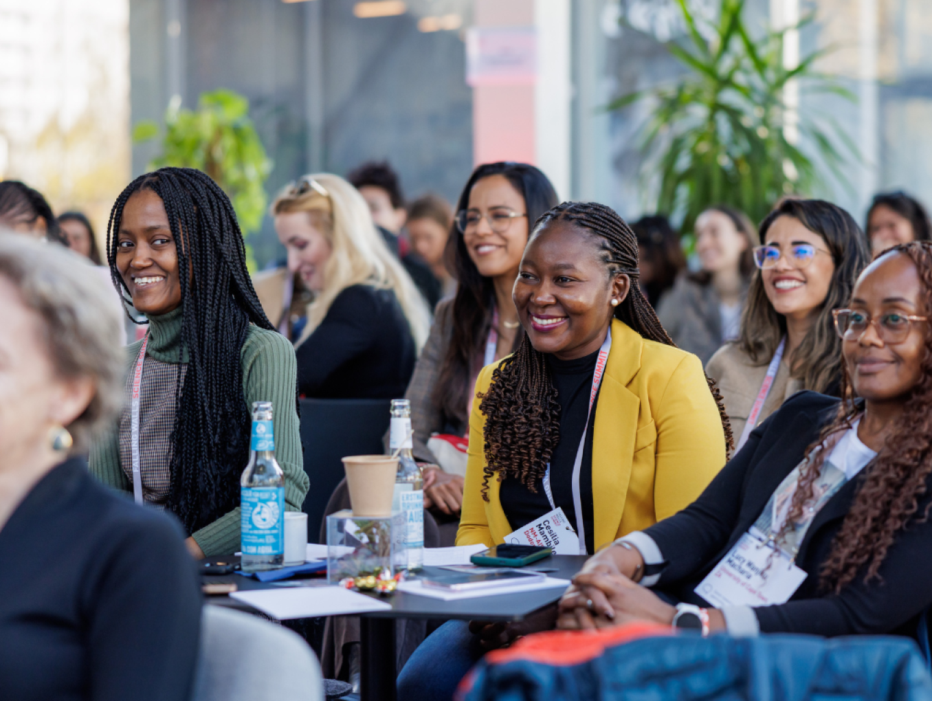 A group of women sitting in the audience together, smiling, and active listening to a speaker off-the-picture.