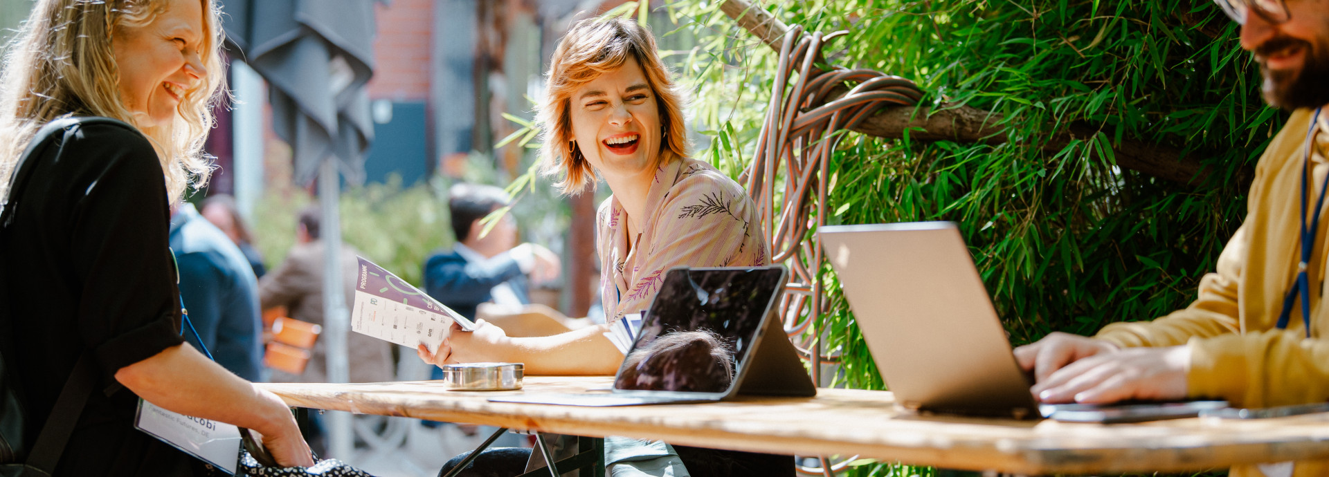 3 people sitting on a table, laughing looking at a laptop 