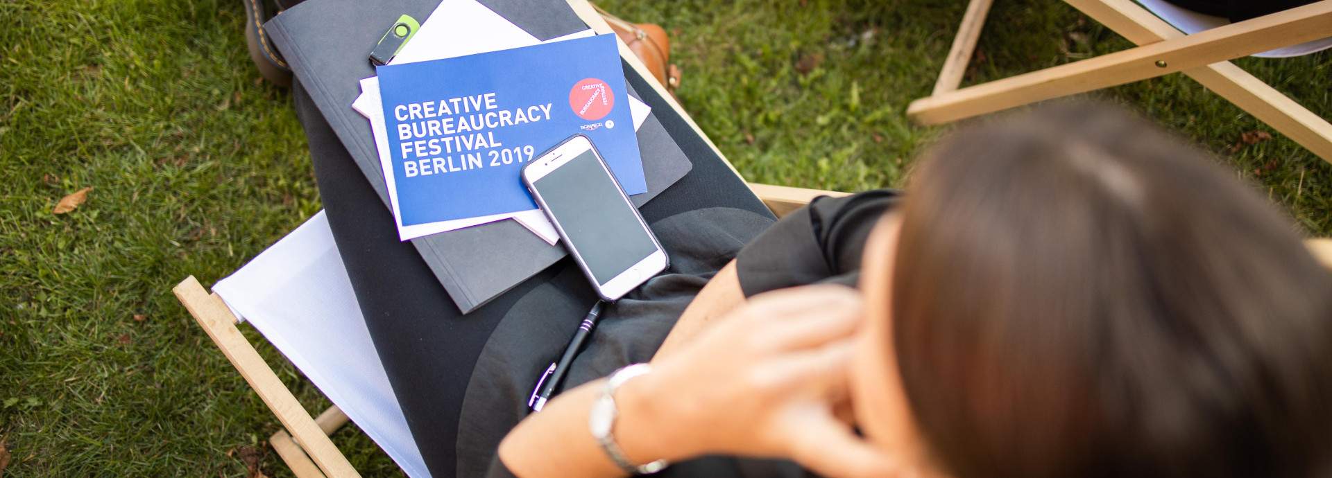 woman sitting outside with a festival 2019 card, papers and phone on her lap