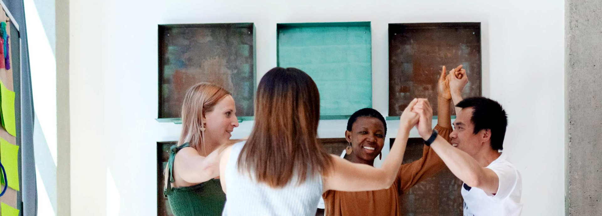 Four people stand in a circle, smiling and raising their hands together in a team activity during a workshop.