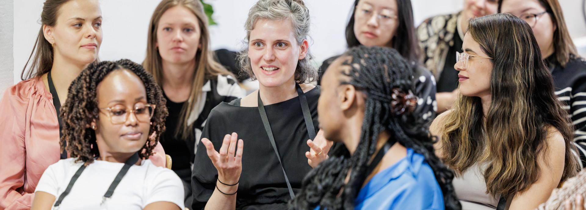 A group of women scientists are sitting in rows. The woman in the middle is speaking. Everyone is listening to her.