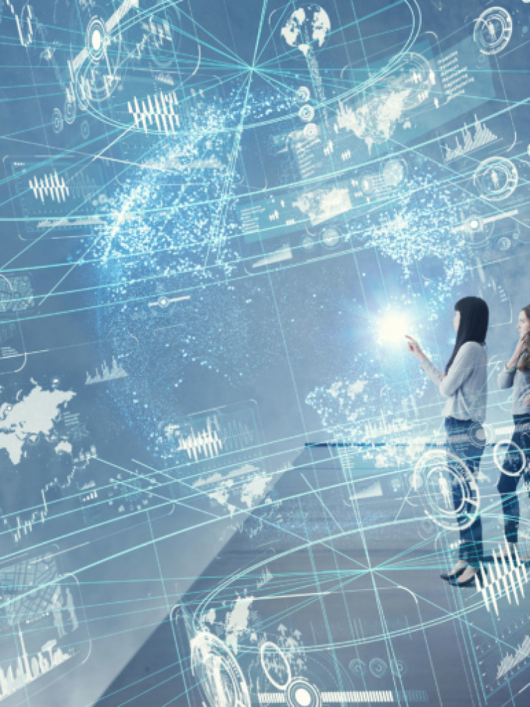 A group of four business professionals, two men and two women, stand in a modern, digitally enhanced environment. They are looking towards a bright, glowing point in a holographic projection that encompasses the room. The projection features a global network of interconnected lines, data points, charts, and world maps, suggesting themes of global communication, technology, and data analysis. The overall color scheme is cool blues and whites, indicating a futuristic and high-tech setting.