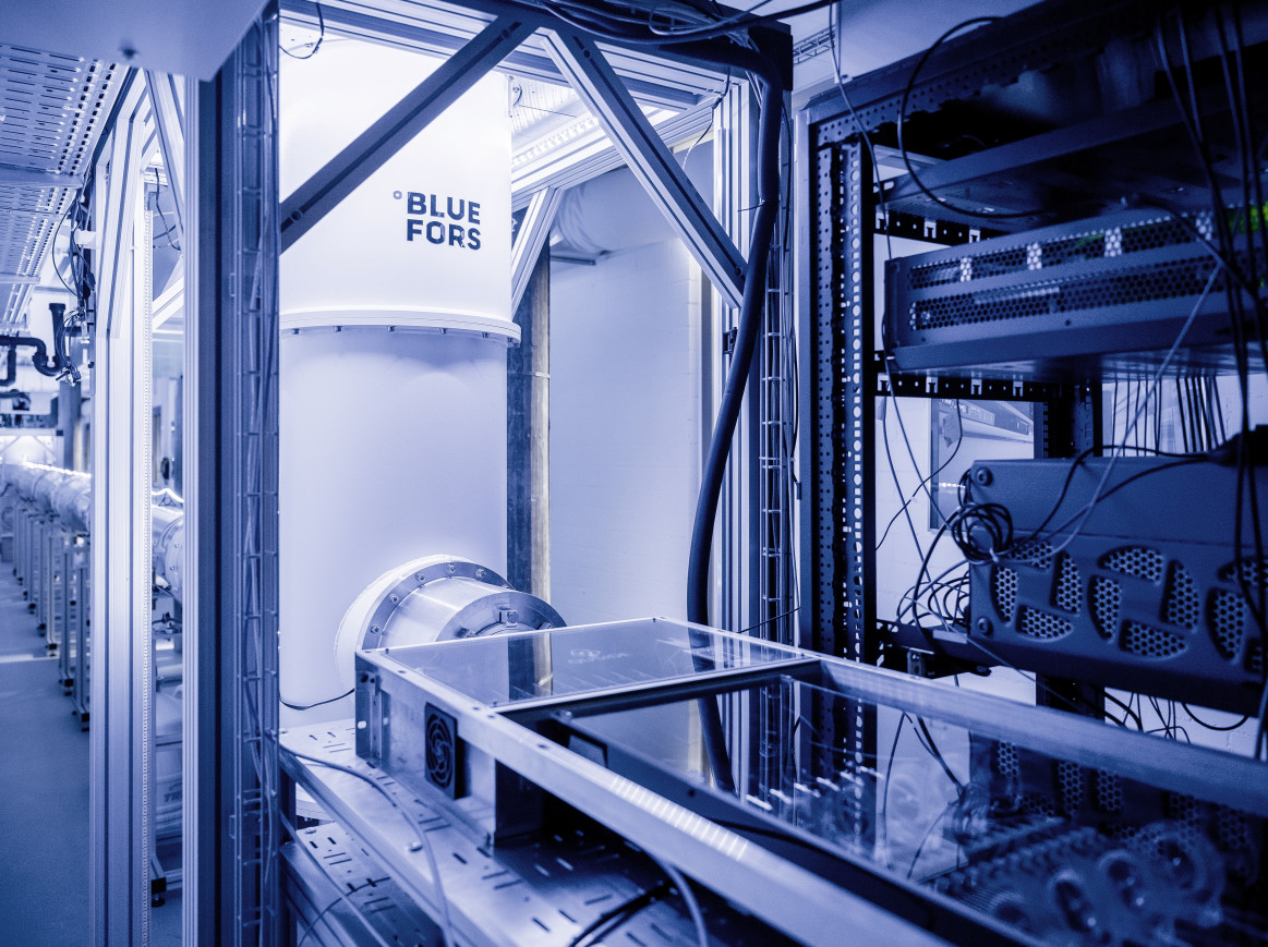 Section of a 30-meter-long cryogenic quantum link (back), allowing for the exchange of quantum information between two dilution refrigerators (front). At room temperature, specialized electronic equipment controls the state of a quantum processor operated in the dilution refrigerator in the front, at temperatures of about 10 millikelvin.