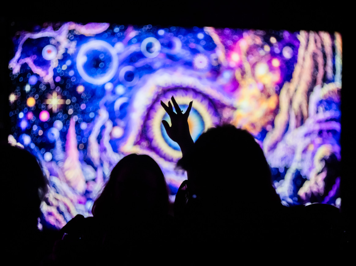 A crowd dancing in front of a screen with ai-generated visuals
