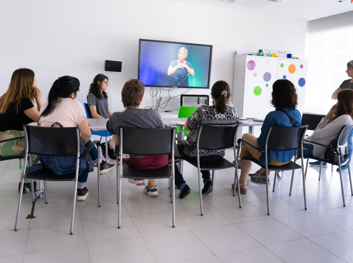 Several women are watching a presentation video on TV together. 