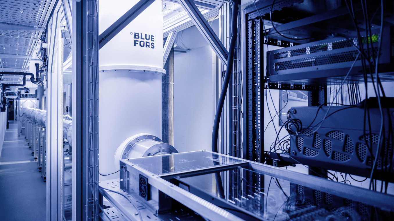 Section of a 30-meter-long cryogenic quantum link (back), allowing for the exchange of quantum information between two dilution refrigerators (front). At room temperature, specialized electronic equipment controls the state of a quantum processor operated in the dilution refrigerator in the front, at temperatures of about 10 millikelvin.