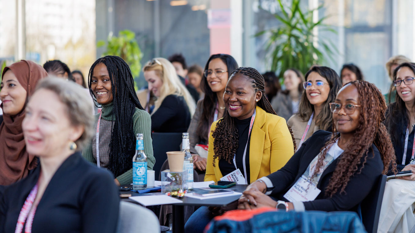 A group of women are sitting in the audience, smiling, looking at the speaker out of frame.